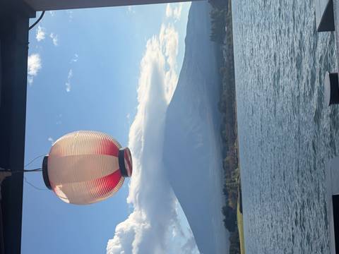       Traditional paper lantern hangs over a lake with cloud-topped Mount Fuji rising beyond.
  