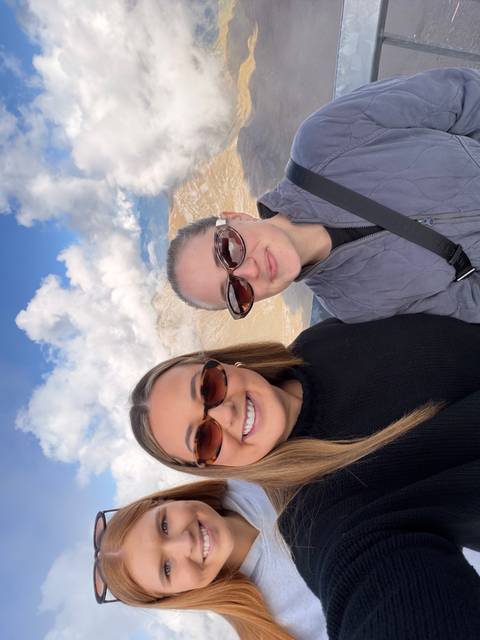       Two smiling women take a selfie with snowy peaks and dramatic clouds behind them.
  