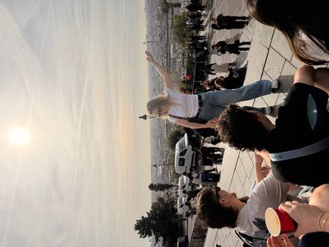       Traveller gestures over Paris skyline from steps of Sacré-Cœur while others relax nearby.
  