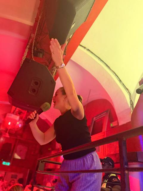      Woman passionately singing into a microphone under vibrant red club lighting.
  