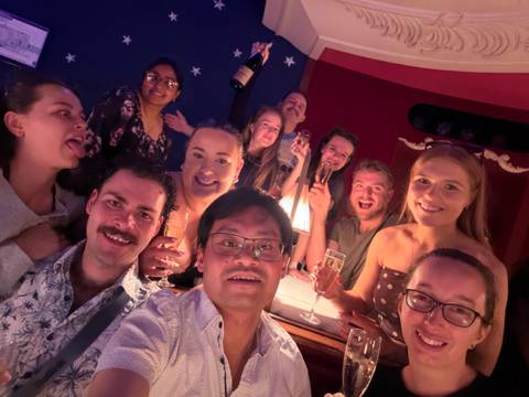       Large group of travellers celebrating indoors with champagne glasses and festive lighting.
  