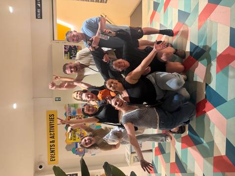       Cheerful group posing inside a hostel lobby area, arms raised in celebration.
  