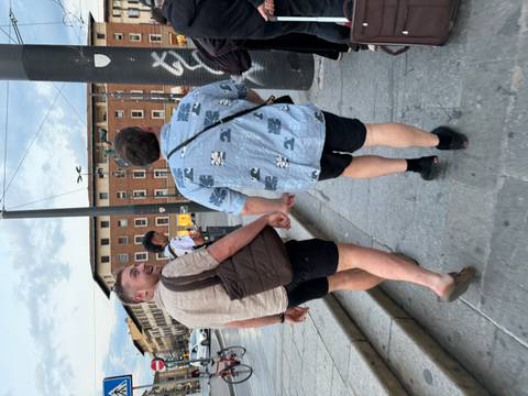       Two men walking hand in hand on a city street in the evening with historic buildings and tram lines.
  