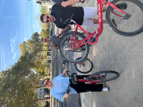       Three travellers with bright red rental bikes posing in a sunny park.
  