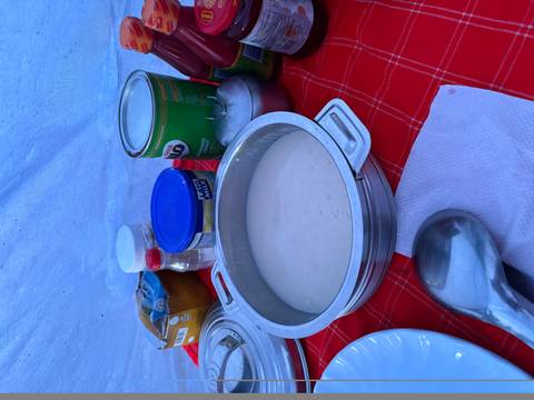       Simple breakfast porridge served in a metal pot on a red checkered tablecloth inside a tent.
  