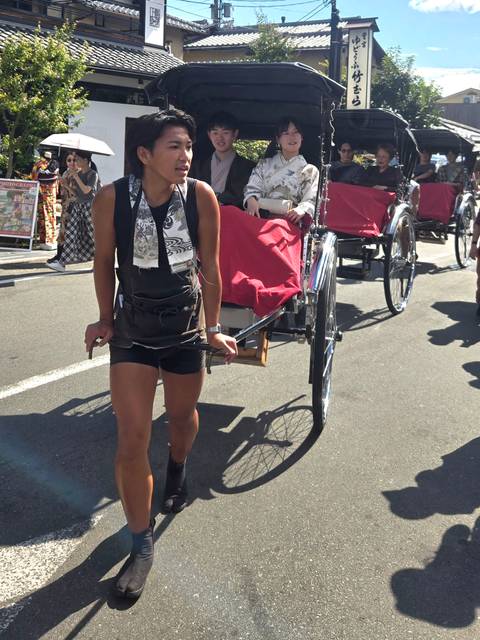       A muscular rickshaw puller strides down a Tokyo street towing passengers in traditional style.
  