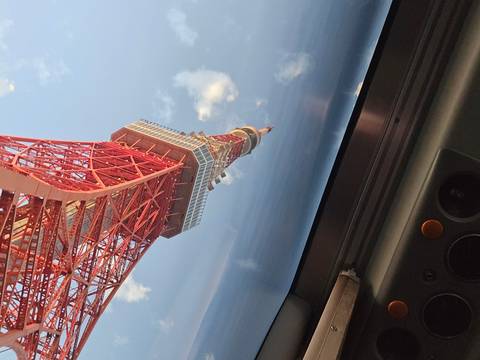       A tilted upward view of the red lattice Tokyo Tower set against a blue sky scattered with clouds.
  