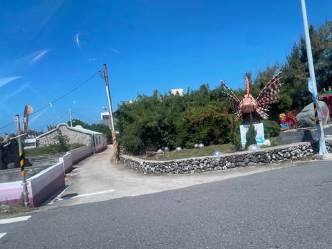       Roadside tropical scene viewed through a car window with decorative fish sculpture.
  