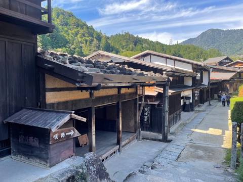       Traditional wooden Edo-era street in a mountain village with visitors exploring.
  