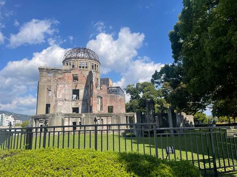       Ruined Atomic Bomb Dome stands solemnly against a bright blue sky and fluffy clouds.
  