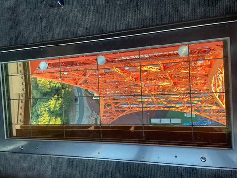      View through a glass floor down the vivid orange steel lattice of Tokyo Tower.
  
