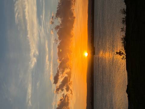       Brilliant orange sun setting over calm sea with scattered clouds.
  
