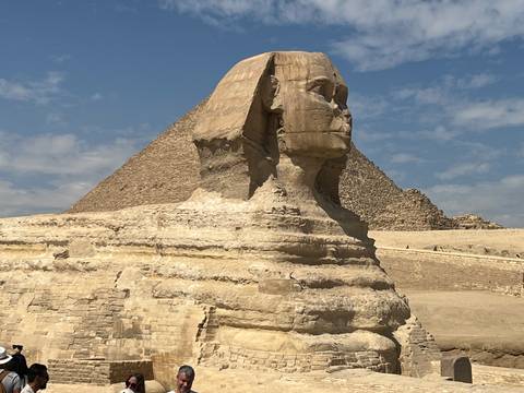       Close-up of the Great Sphinx with the Pyramid of Khafre rising behind under a partly cloudy sky.
  
