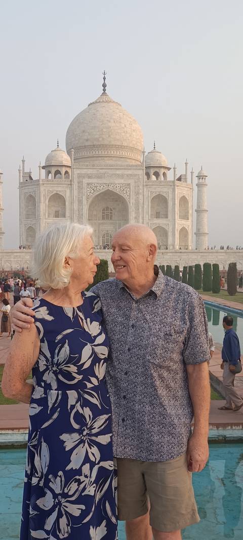       Elderly couple share a loving look with the Taj Mahal’s marble façade and reflecting pool behind them.
  
