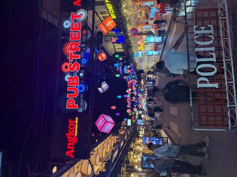       Neon-lit Pub Street in Siem Reap buzzes with people and colorful hanging cubes at night.
  