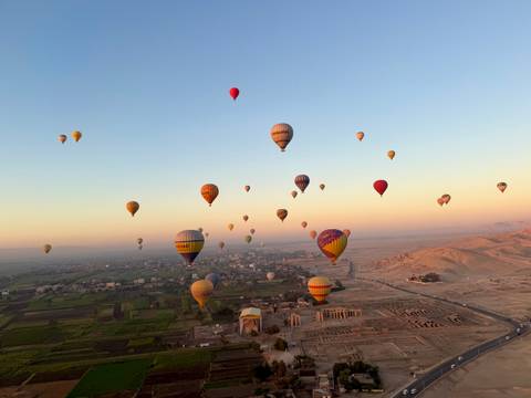       Dozens of colourful hot-air balloons float above temples and farmland of Luxor at dawn.
  