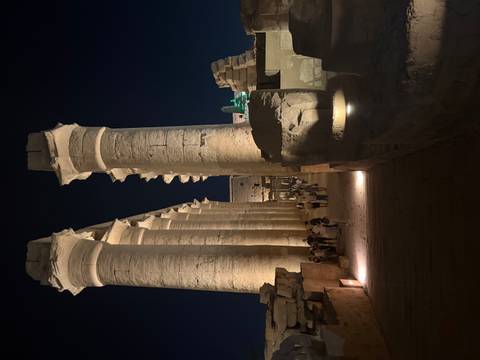       Massive floodlit columns of Luxor Temple glow against night sky as visitors stroll along walkway.
  