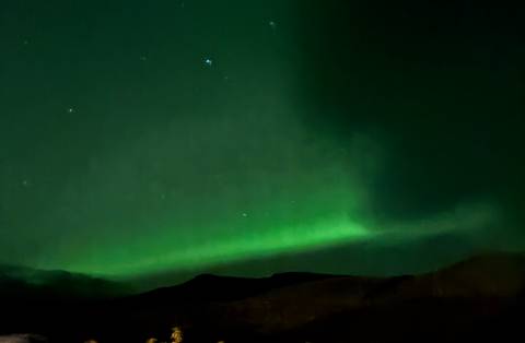       Soft green aurora borealis glowing above dark mountain silhouettes in the night sky.
  