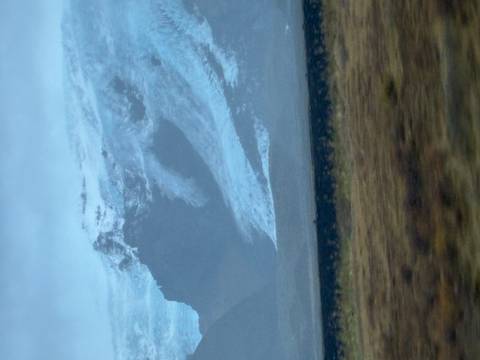       Blurry view of a glacier-covered mountain taken from a moving vehicle on an overcast day.
  