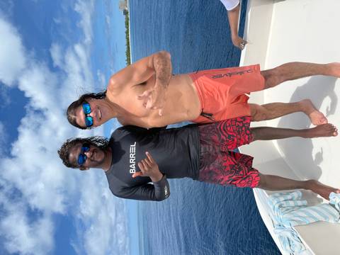       Two friends wearing sunglasses pose on a boat deck with deep-blue sea in the background.
  