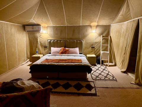      Comfortable desert glamping tent interior with a double bed, carpets and soft lighting.
  