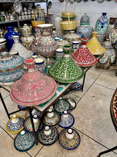       Vibrant painted ceramic tagines displayed on a market table.
  