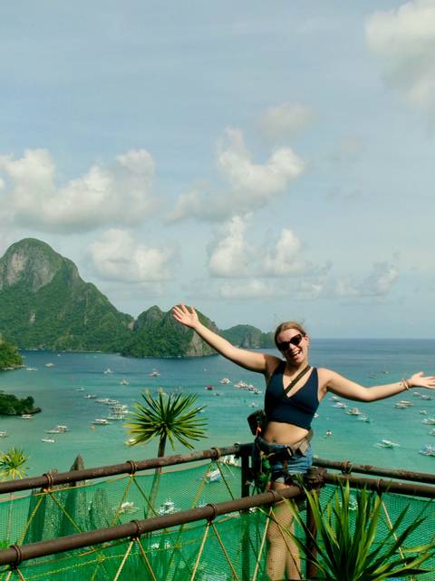       Happy traveler spreads her arms wide at a hilltop viewpoint overlooking emerald bays and dramatic karst islands.
  