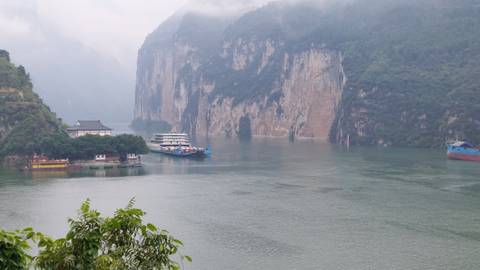       Foggy gorge with towering limestone cliffs and cruise vessels moored along the river.
  