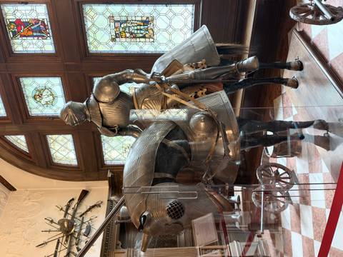       Museum display of an armored knight on horseback behind glass in a grand hall.
  