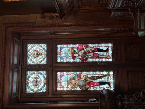       Richly carved wooden doorway featuring colorful stained-glass panels of Renaissance figures.
  