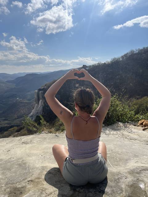 Tilted image of a person posing with heart shape in a scenic outdoor setting.