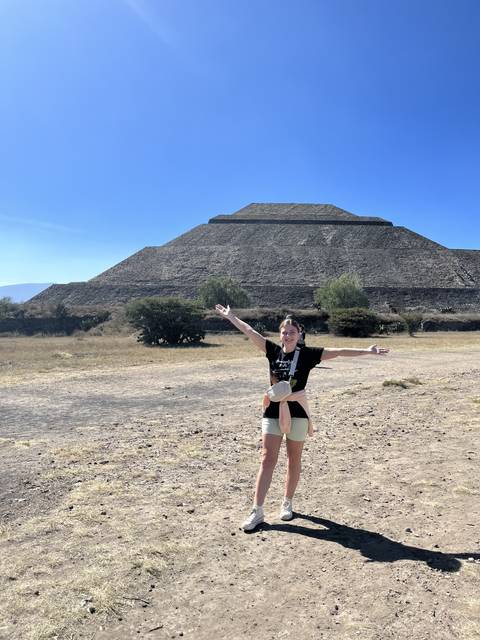 Tilted image of a person posing in front of a large pyramid.