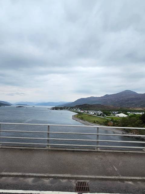       Coastal landscape with road and mountains near a body of water.
  