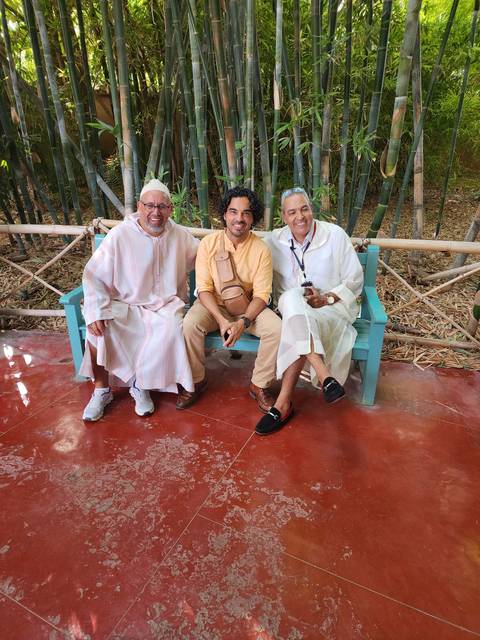       Three people sitting on a bench in a garden setting.
  