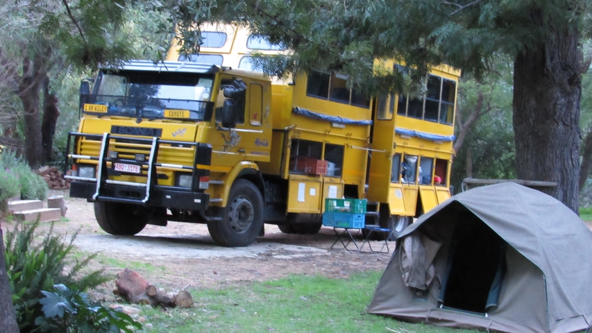       Large overland safari vehicle parked near a tent in a wooded area.
  