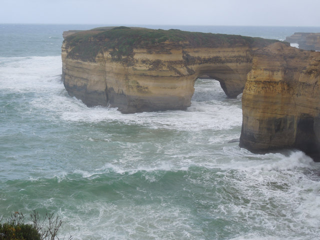       A rock formation with an arch along the coast with waves crashing.
  