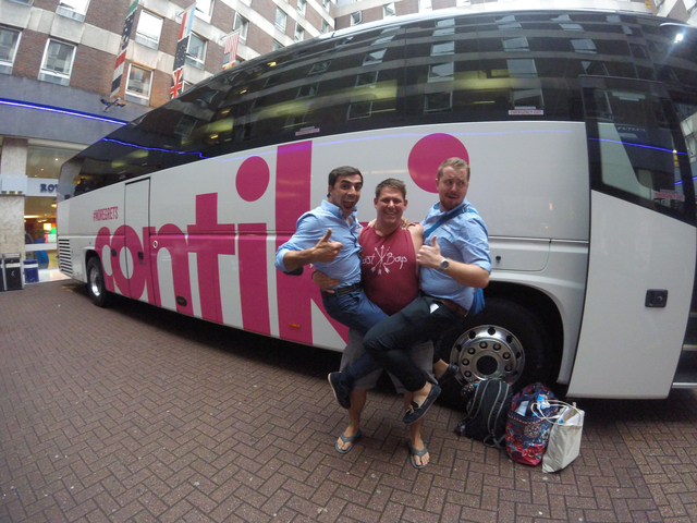 Three people posing in front of a bus with 'contiki' branding.