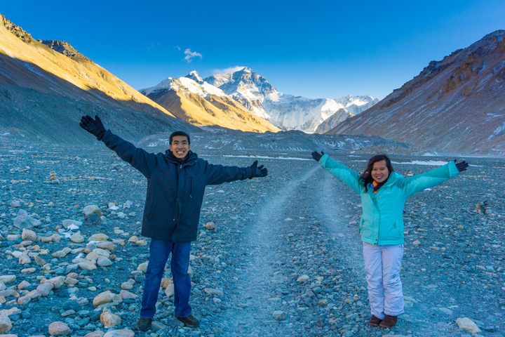 Two people posing with arms outstretched in a mountainous landscape.