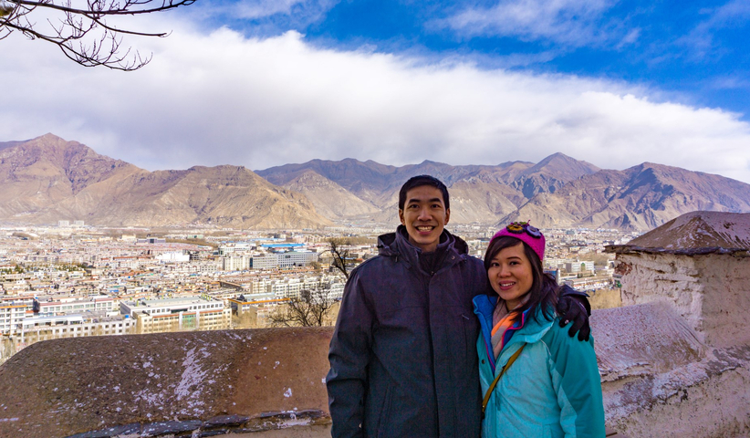 Two people posing with a town and mountains in the background.