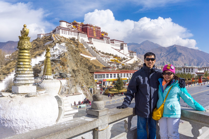 Two people posing in front of a large white building on a hill.