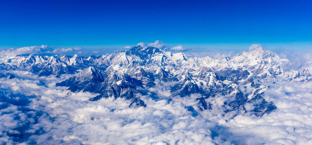 Majestic mountain range with clouds in a clear blue sky.