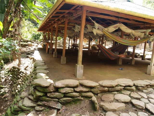       People relaxing in hammocks under a wooden shelter.
  
