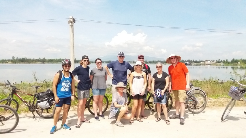       Group of people with bicycles near a water body.
  