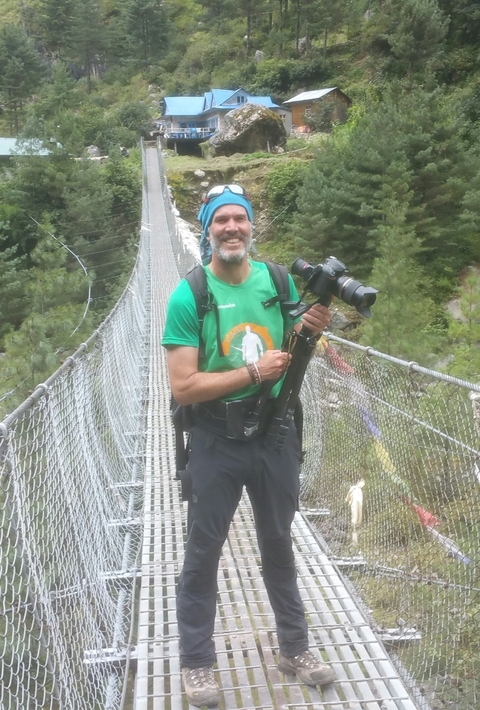       Man standing on a suspension bridge with a camera.
  