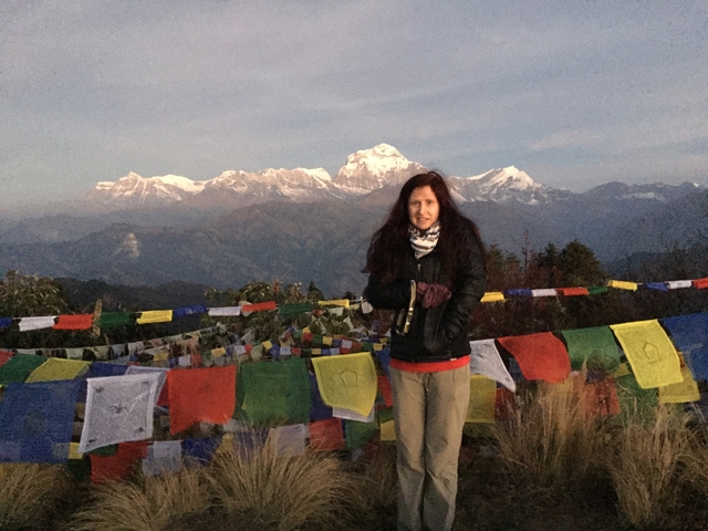 Person standing with prayer flags and mountains in the background.