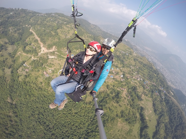 Two people paragliding over a lush landscape.