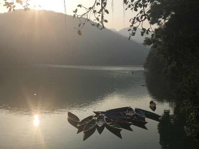 Serene lake with boats and a foggy backdrop.