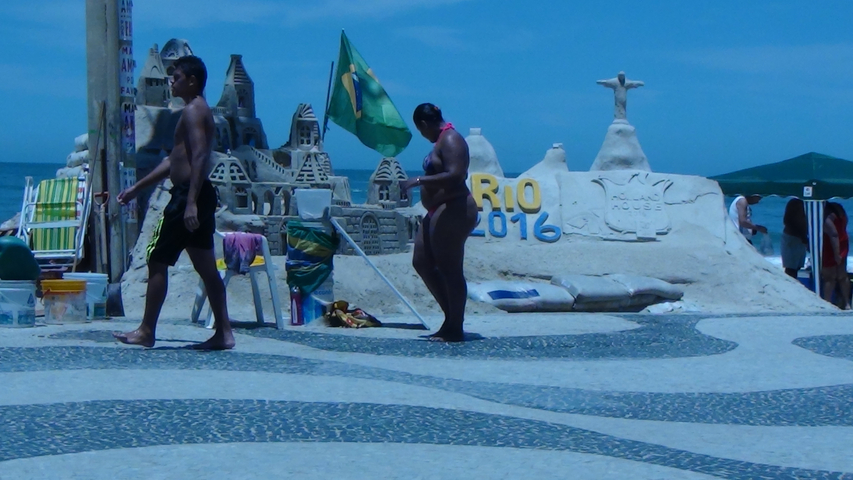 People walking near a sand sculpture labeled 'RIO 2016'.