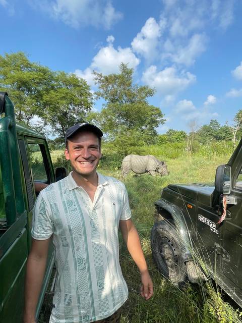 Person smiling near a rhino and safari vehicle.