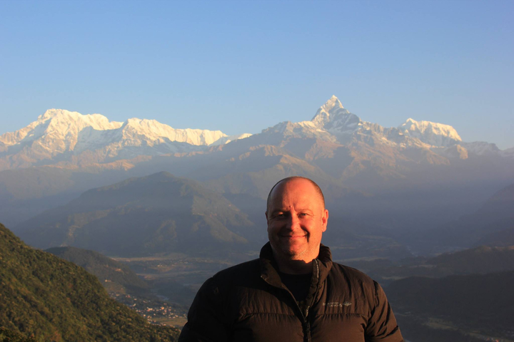       Person posing with a backdrop of Himalayan mountains.
  
